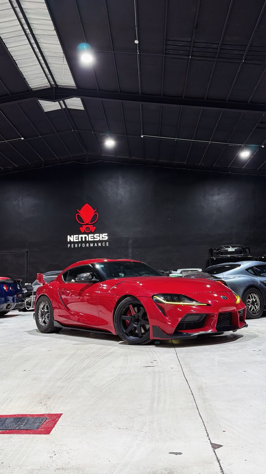 Red Toyota Supra parked under the Nemesis Performance logo wall