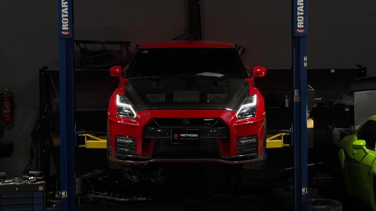 Red Nissan GT-R with Nemesis Performance front plate raised on a workshop lift